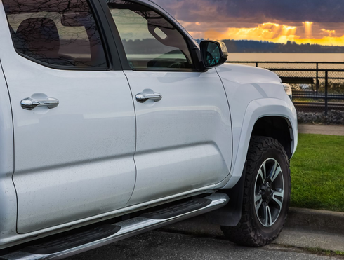 White pickup truck parked by a curb at sunset near water and a railing