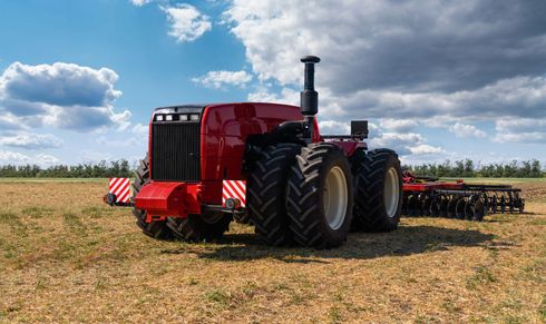 Red tractor with implements parked in a dry field under a partly cloudy sky