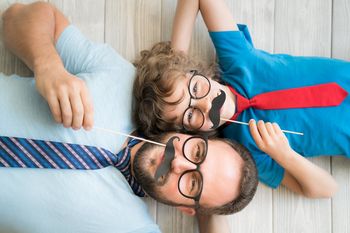 Two smiling people lying on a wooden floor, wearing glasses, with red and blue ties.