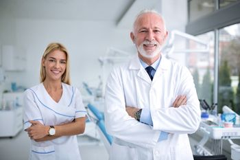 Two smiling lab professionals in white coats standing with arms crossed in a bright laboratory