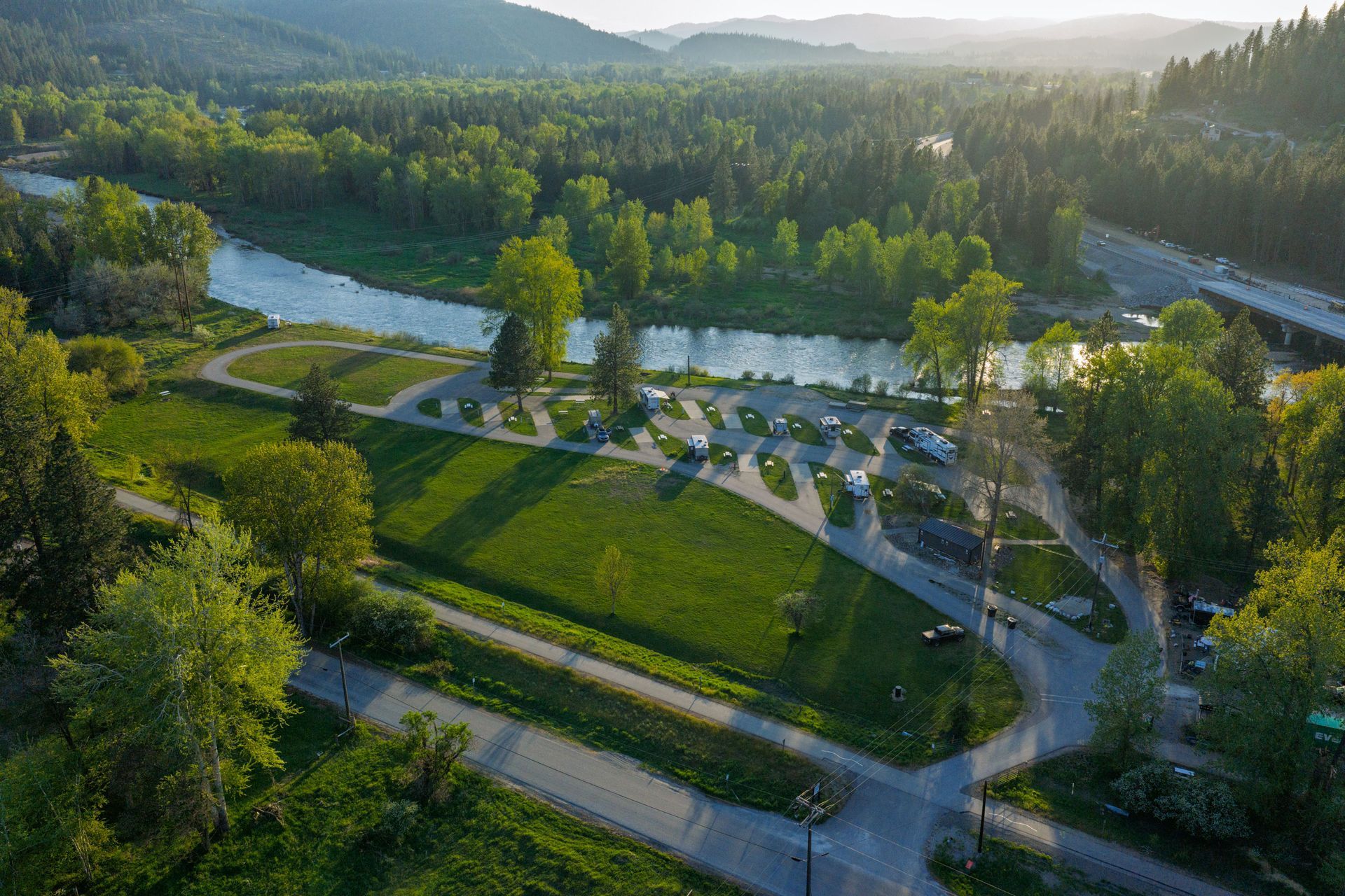 Aerial view of a park with winding paths, a river, and trees at sunset