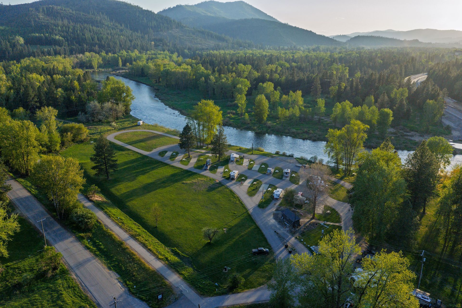 Aerial view of a riverside park with a parking lot, winding river, and forested hills at sunset