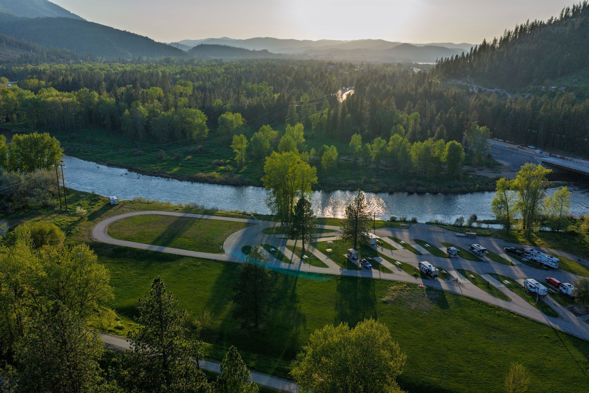 Aerial view of a river winding through a green valley at sunset, with a park and parking lot in the foreground