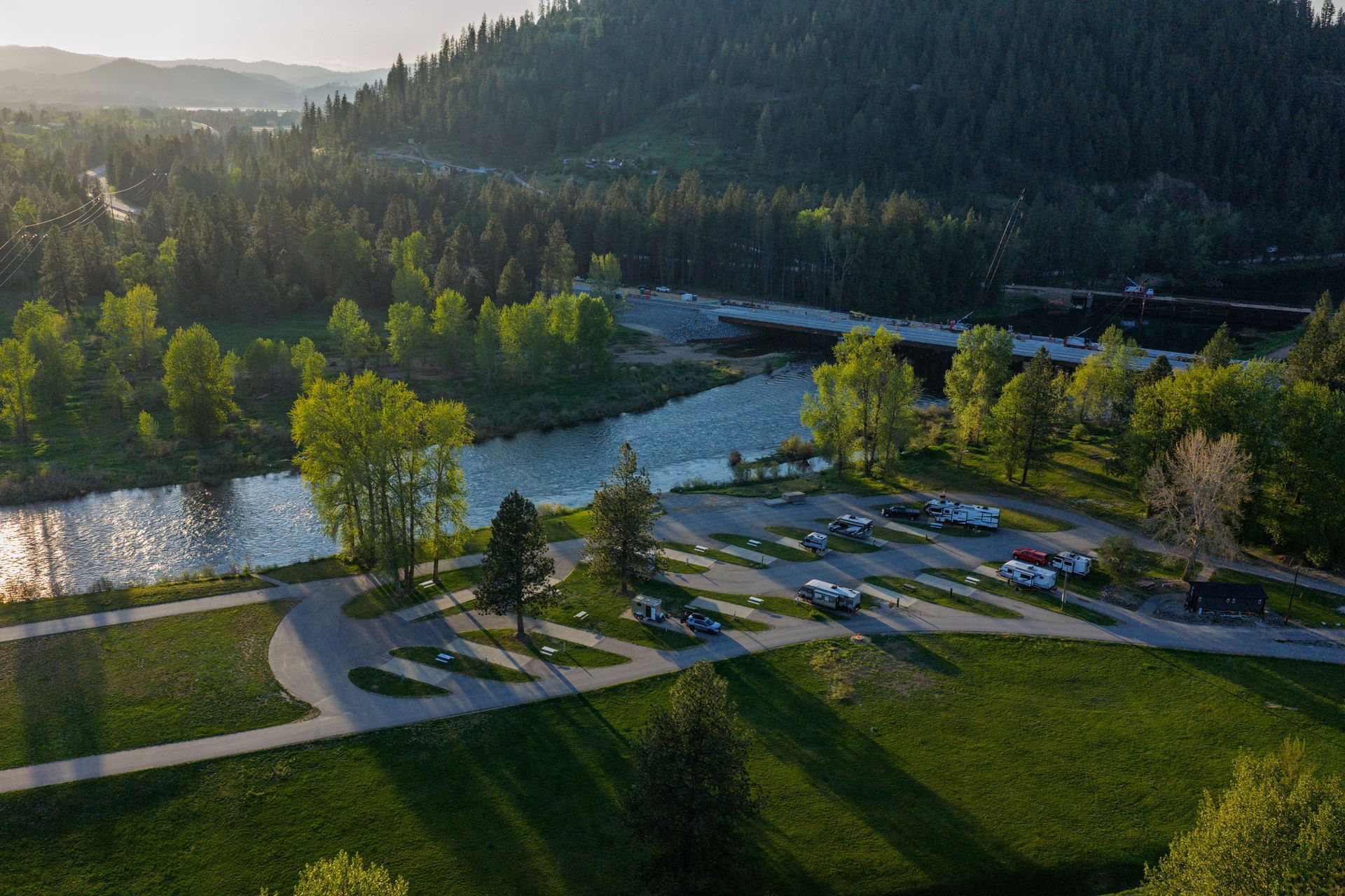 Aerial view of a river bend, trees, parking lot, and walking paths beside a forested hill at sunset