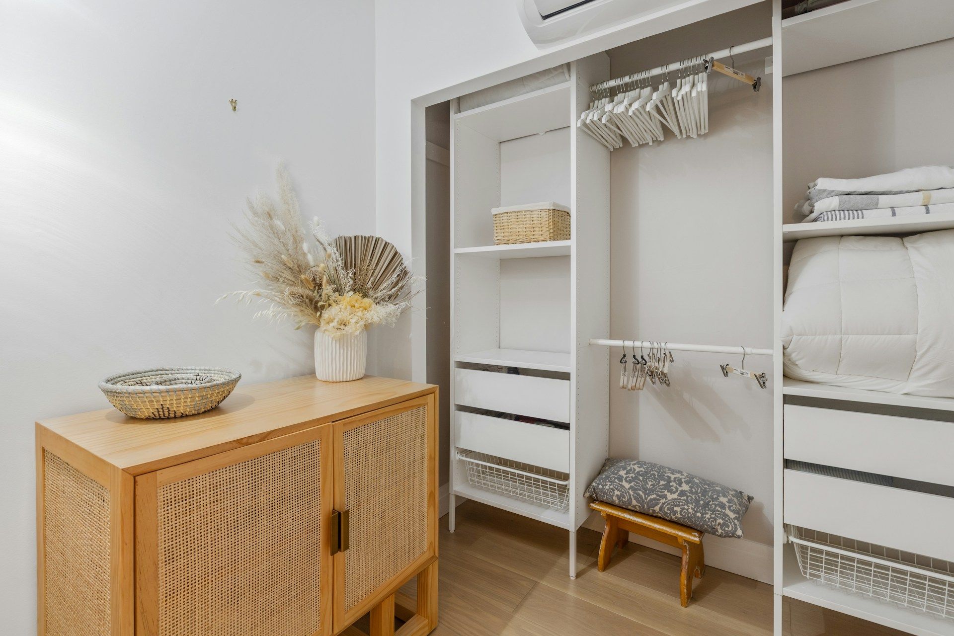 A walk in closet with a wicker cabinet and a stool.