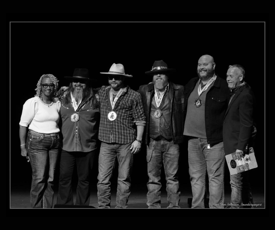 Six people posing on a stage, two wearing medals, in black and white.
