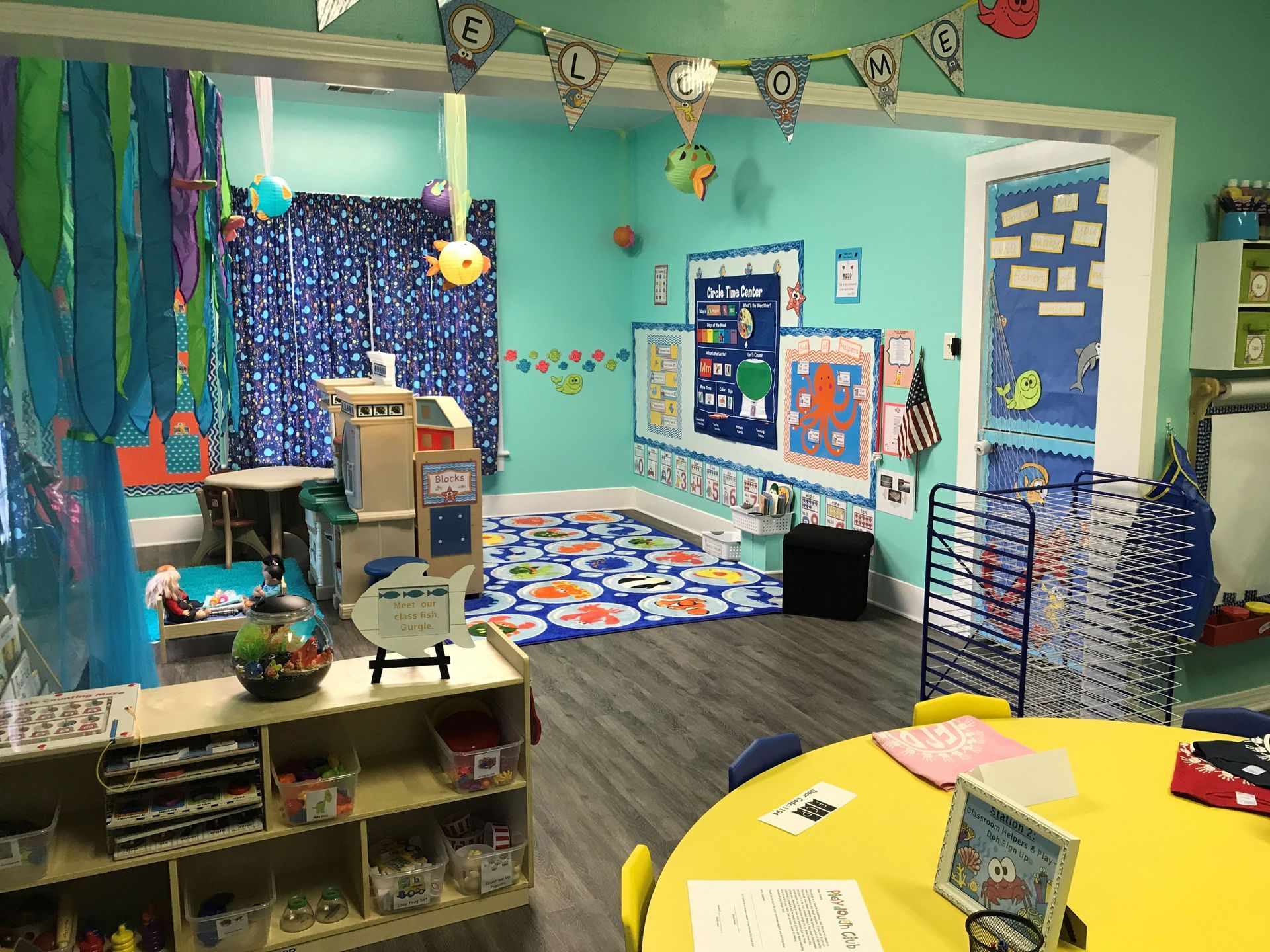 A classroom with a yellow table and chairs and a blue wall.