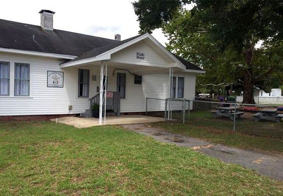 A white house with a black roof and a picnic table in front of it.