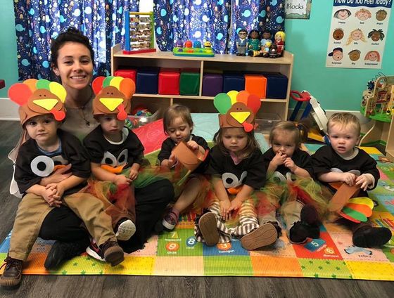 A group of children are sitting on the floor wearing turkey hats.