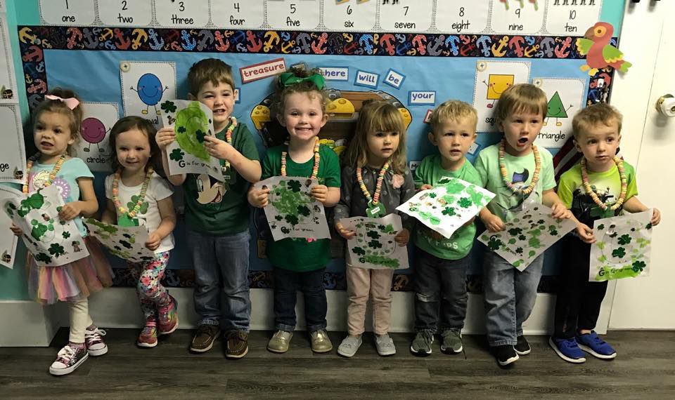 A group of children are standing next to each other in front of a bulletin board.