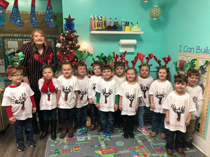 A group of children wearing reindeer antlers are posing for a picture in front of a christmas tree. A group of children wearing reindeer antlers are posing for a picture in front of a christmas tree.