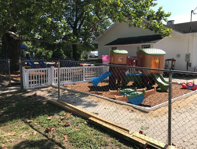 A chain link fence surrounds a playground with a house in the background.