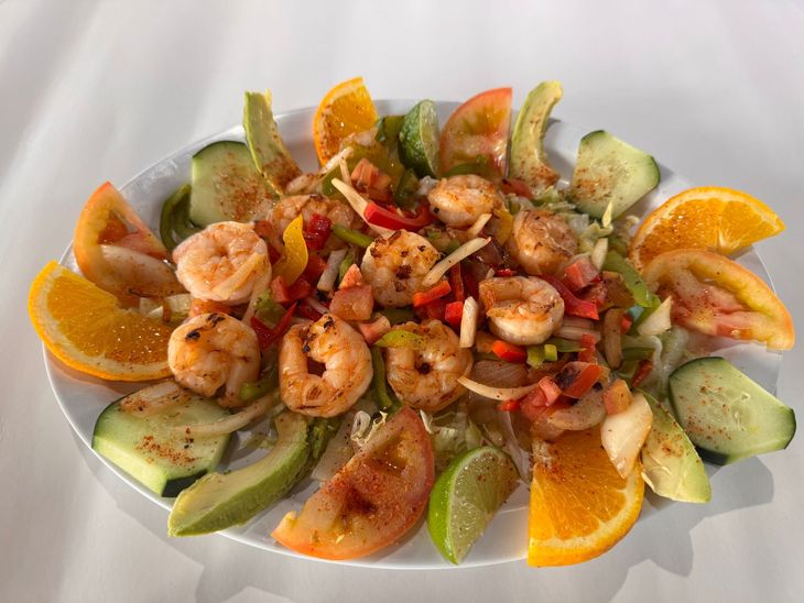 Shrimp salad with avocado slices, orange wedges, and chopped peppers on a white plate