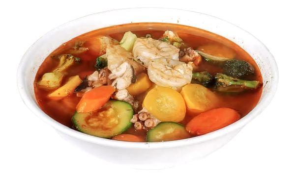 Clear bowl of chicken vegetable soup with carrots, zucchini, potatoes, and herbs in red broth