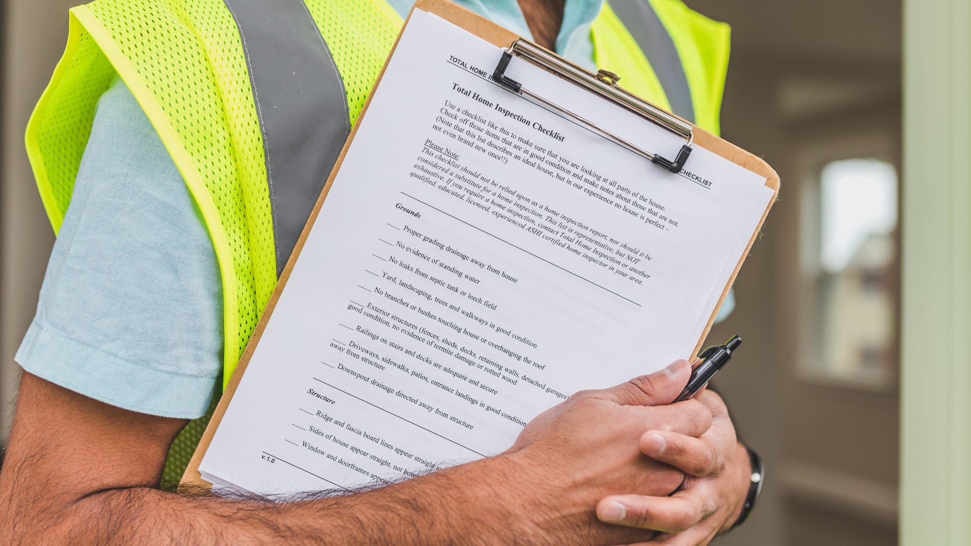 A person in a high-visibility vest holds a clipboard with a checklist while standing in a building under construction.