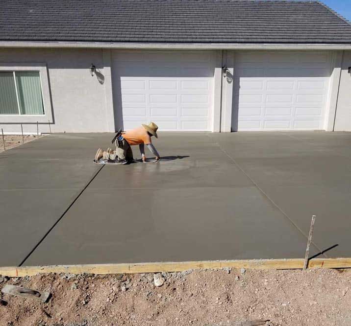 A man is working on a concrete driveway in front of a house.
