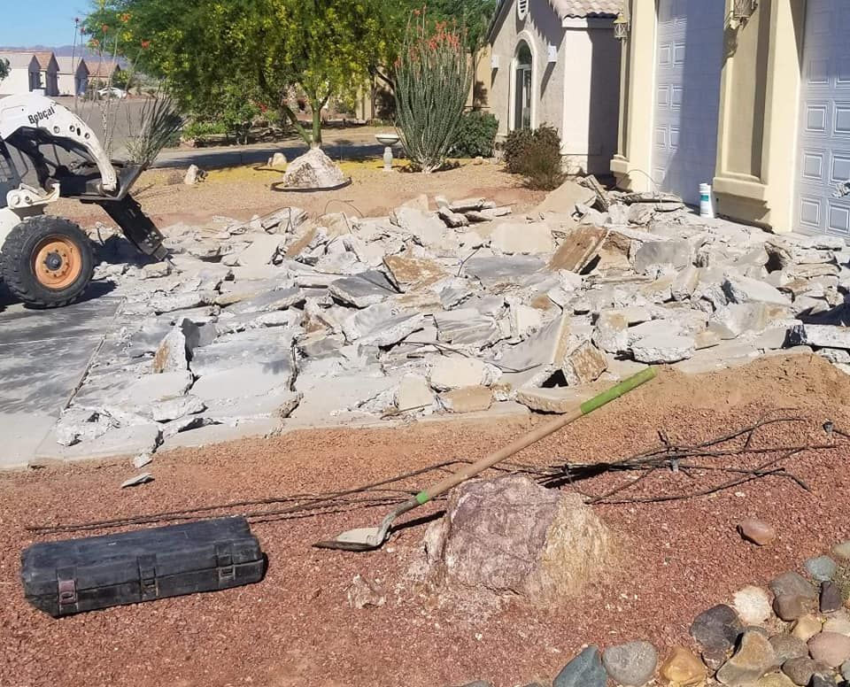 A bobcat is demolishing a driveway in front of a house.