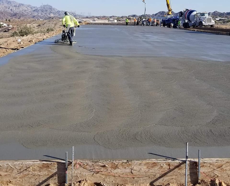 A concrete road is being poured with a crane in the background