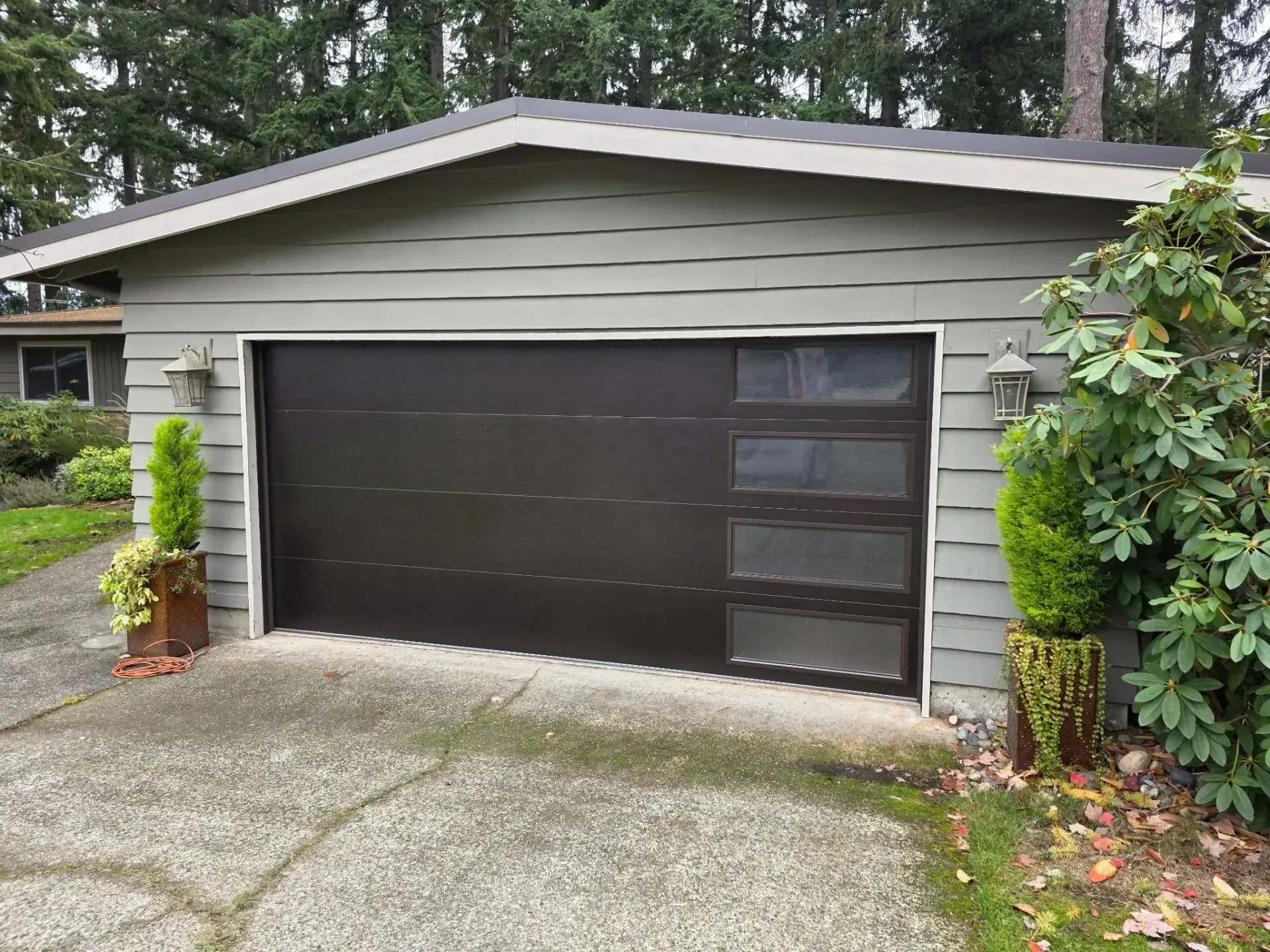 A detached garage with gray horizontal siding and a dark brown garage door featuring a vertical stack of four windows.