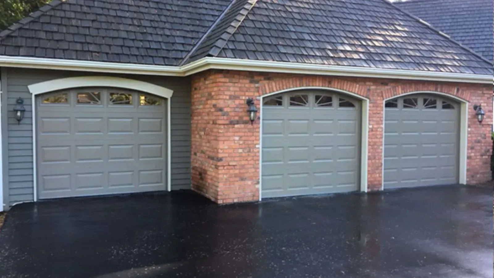 A three-car garage with arched gray doors, a brick and siding exterior, and a dark shingled roof.