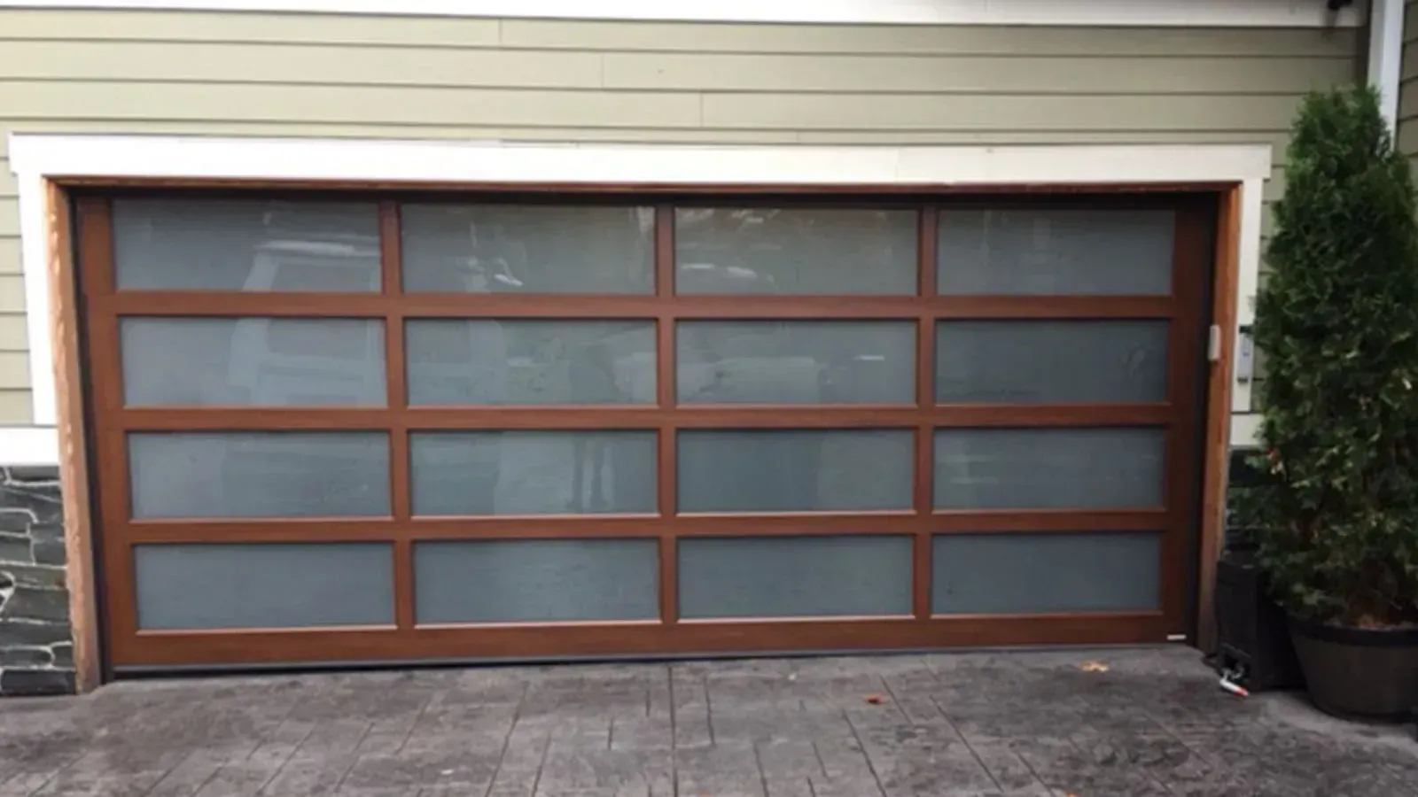 A modern garage door with a brown frame and horizontal rows of frosted glass windows installed in a residential home.