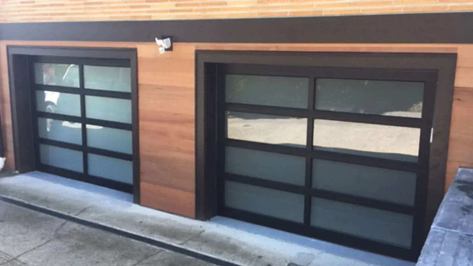 Two modern garage doors with horizontal wood siding, black frames, and frosted glass panels.