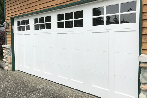 A white, multi-panel residential garage door with top-row windows, set against a house with light wood siding.