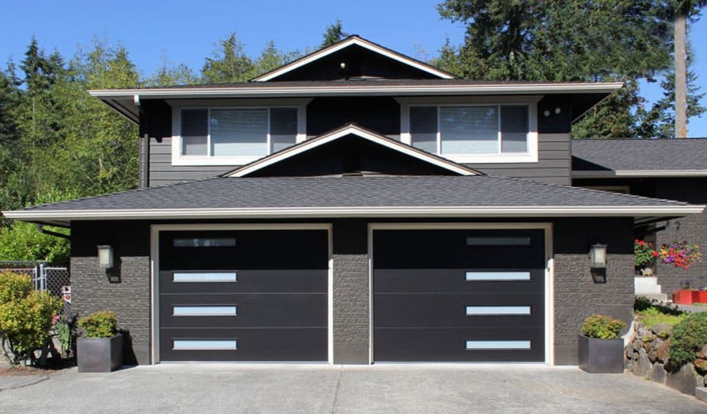 Two-story house with dark gray horizontal siding, a wide asphalt driveway, and two modern black garage doors with windows.