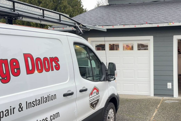A white garage door repair service van parked in a driveway in front of a white garage door.