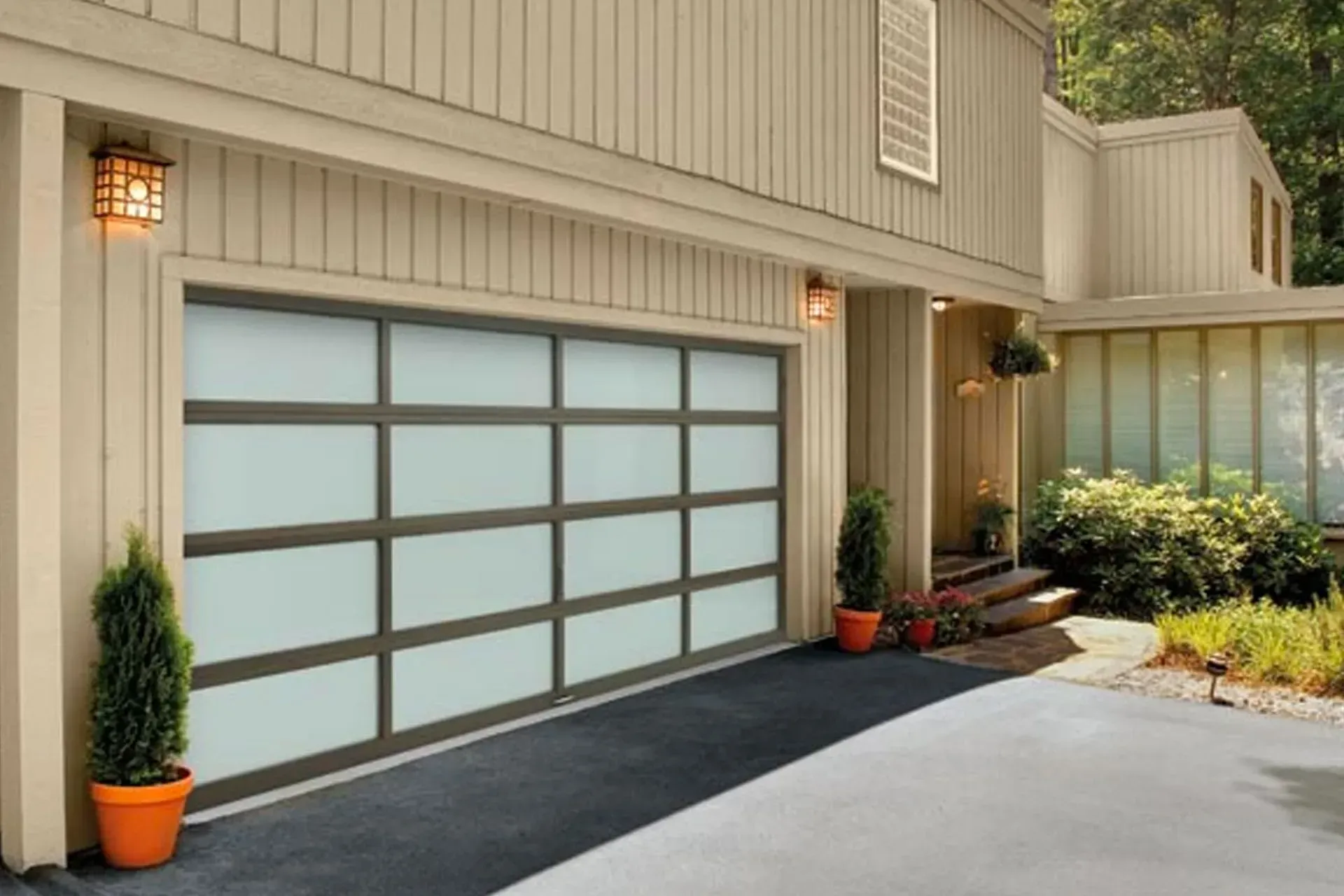 A modern, tan-sided house with a large, glass-paneled garage door featuring a dark frame.