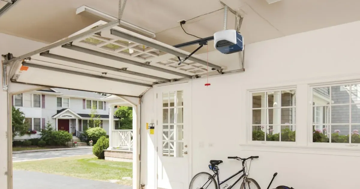 A view from inside a garage looking out at a residential street, with a bicycle parked against a white interior wall.