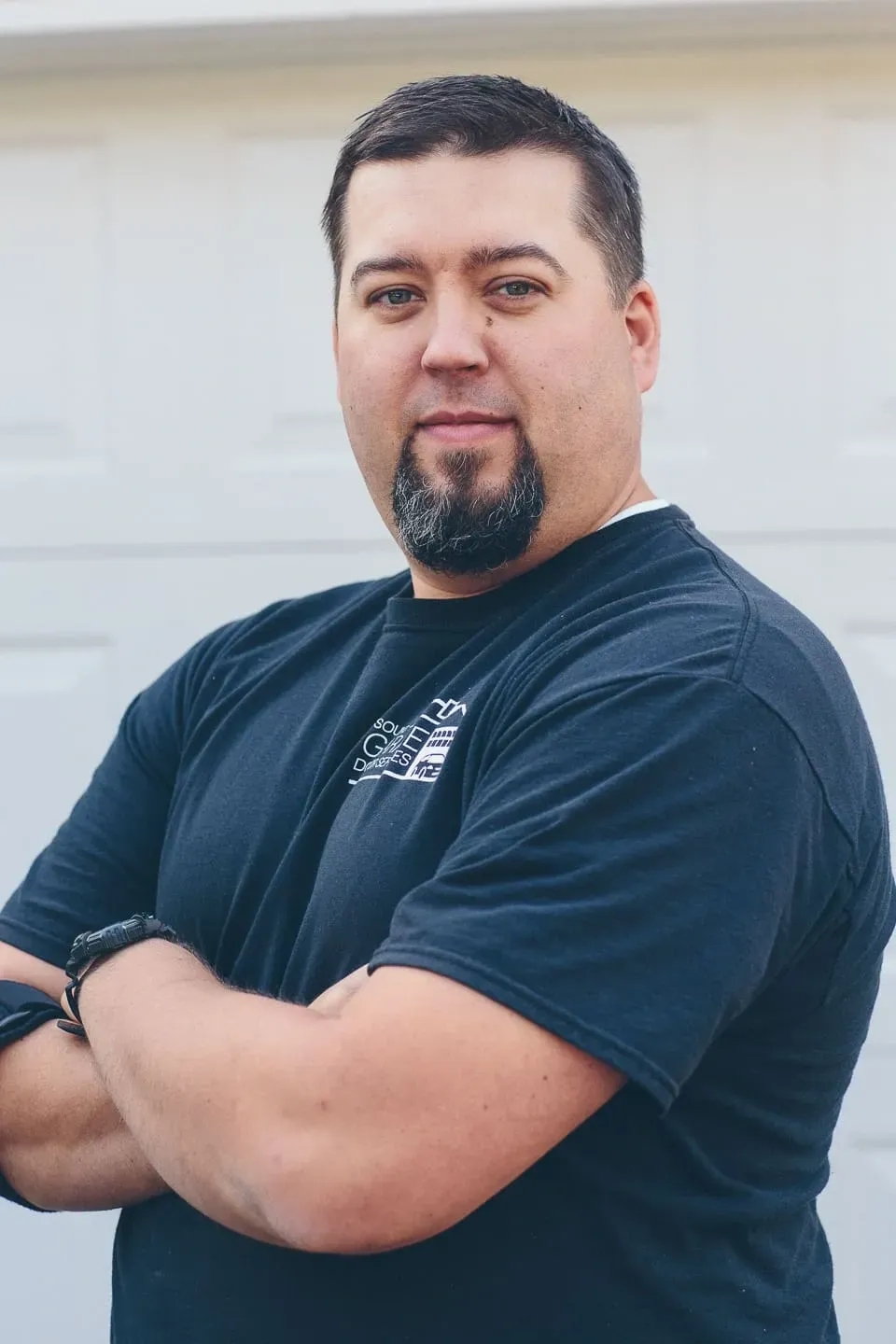 A Sound Door Services technician with a goatee and short brown hair stands with arms crossed.