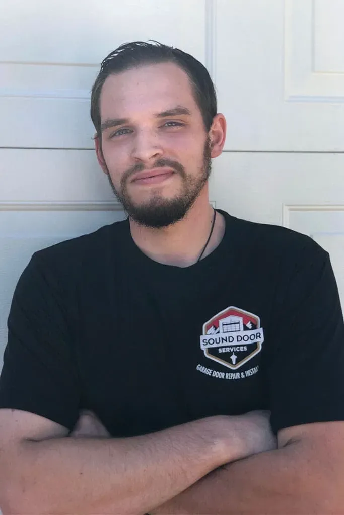A Sound Door Services technician with a beard and dark hair wearing a black t-shirt with a company logo.