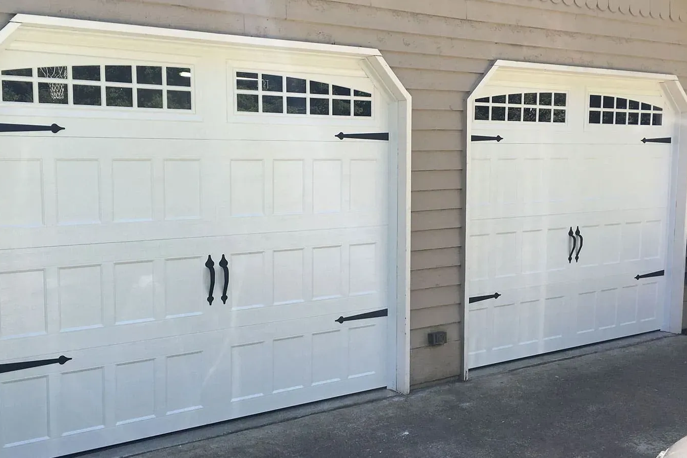Two white carriage-style garage doors with windows at the top and black decorative hinges and handles.