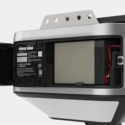 Close-up of an open compartment in a silver garage door opener housing, showing a rectangular backup battery inside.