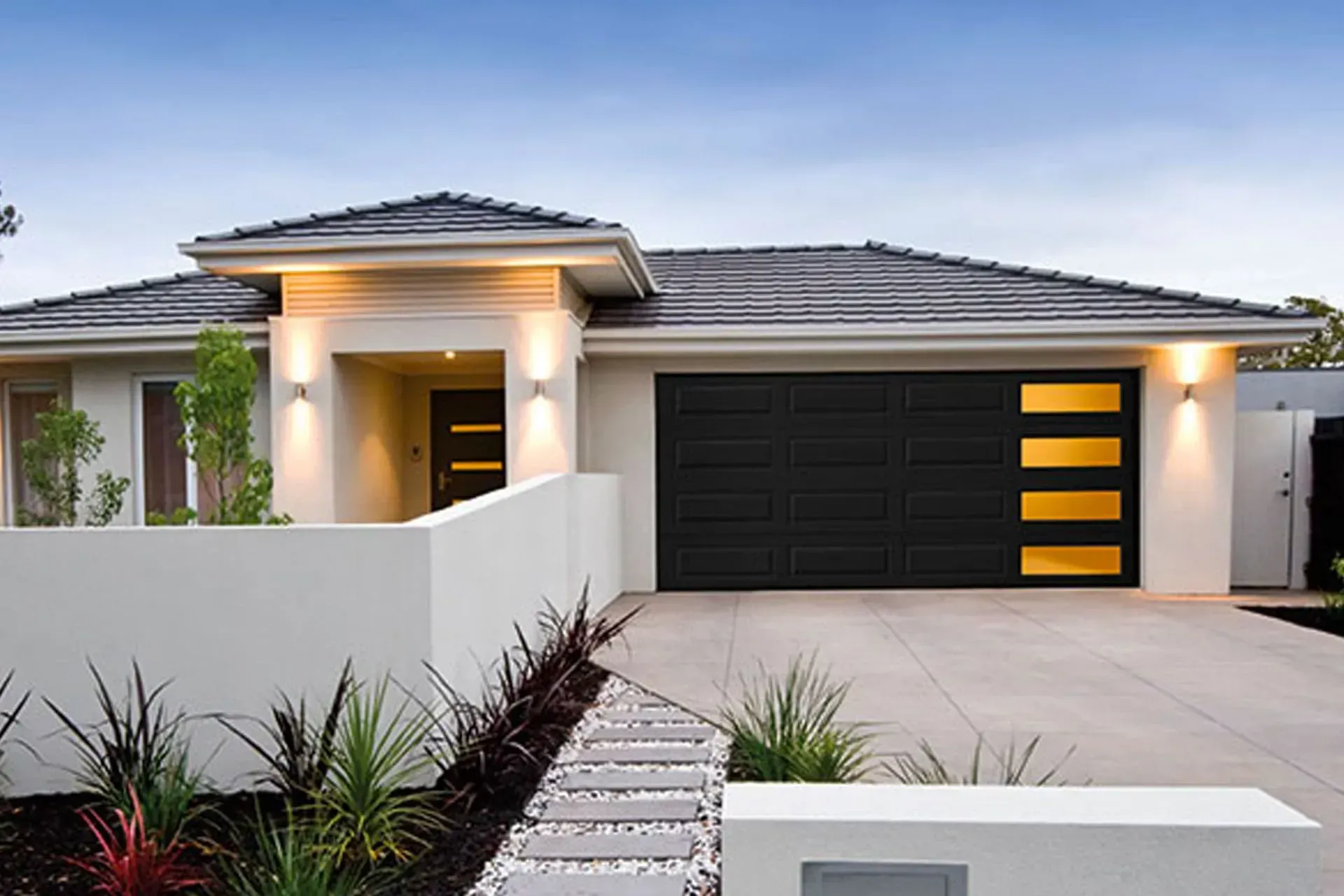 A modern single-story house with a white exterior, a dark gray garage door, and a stone walkway in a landscaped yard.