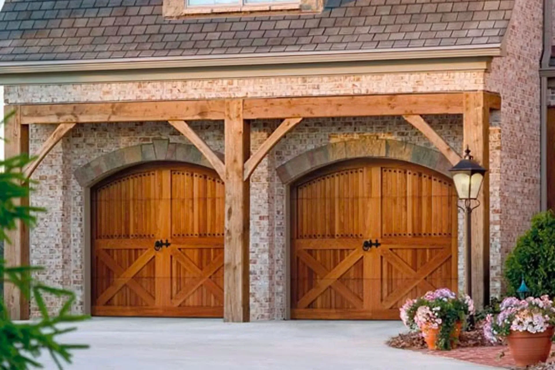 A double garage with arched, wood carriage-style doors under a rustic timber pergola and brick facade.