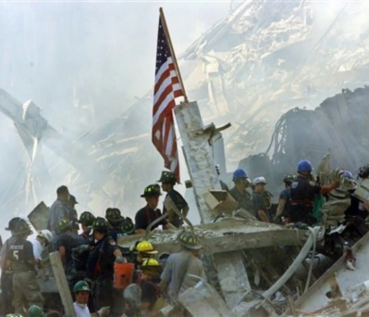 Rescue workers amid World Trade Center rubble, with a U.S. flag raised in the foreground.