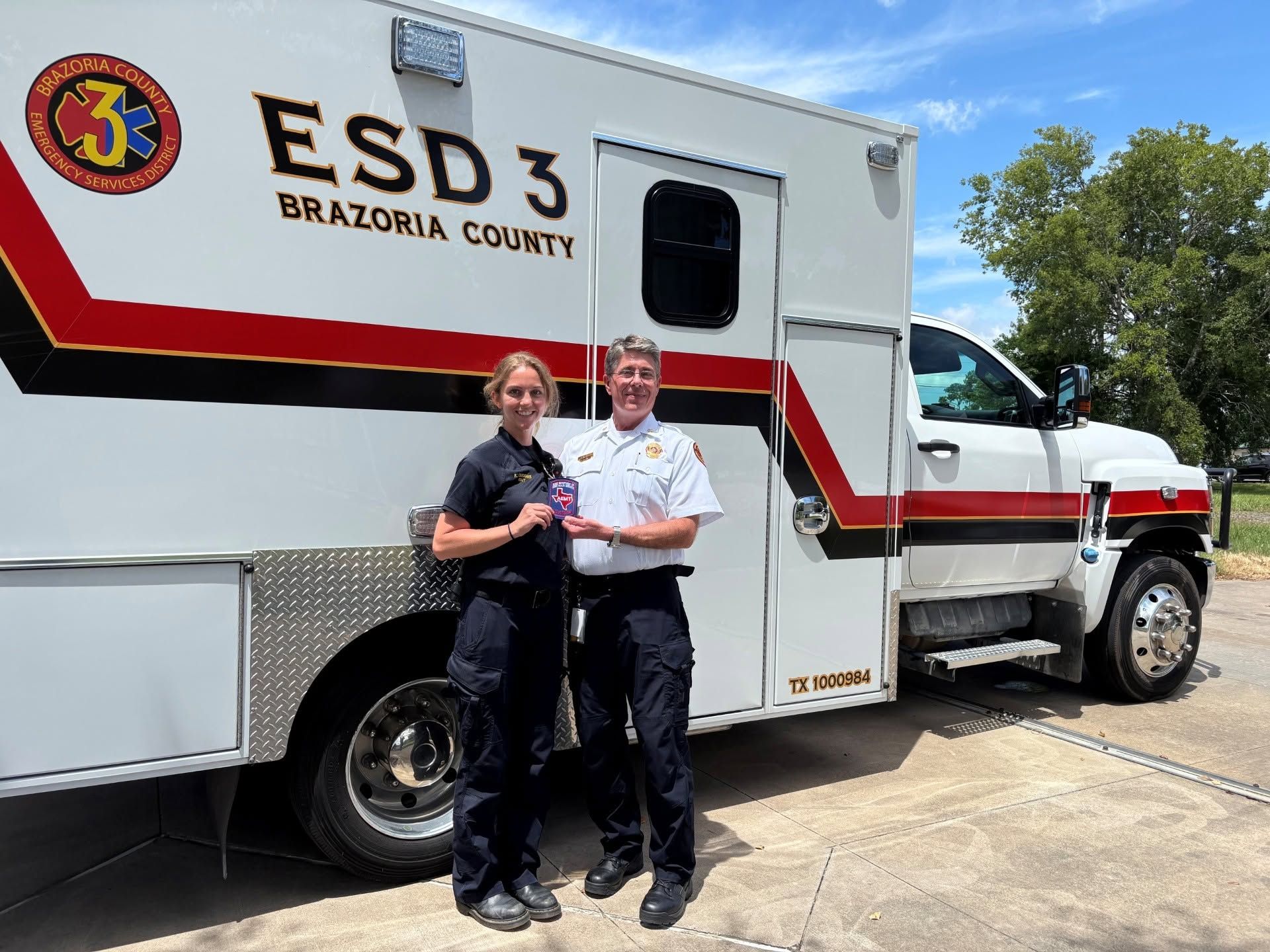 Two people in dark shirts standing beside a white emergency vehicle labeled “ESD 3 Brazoria County”