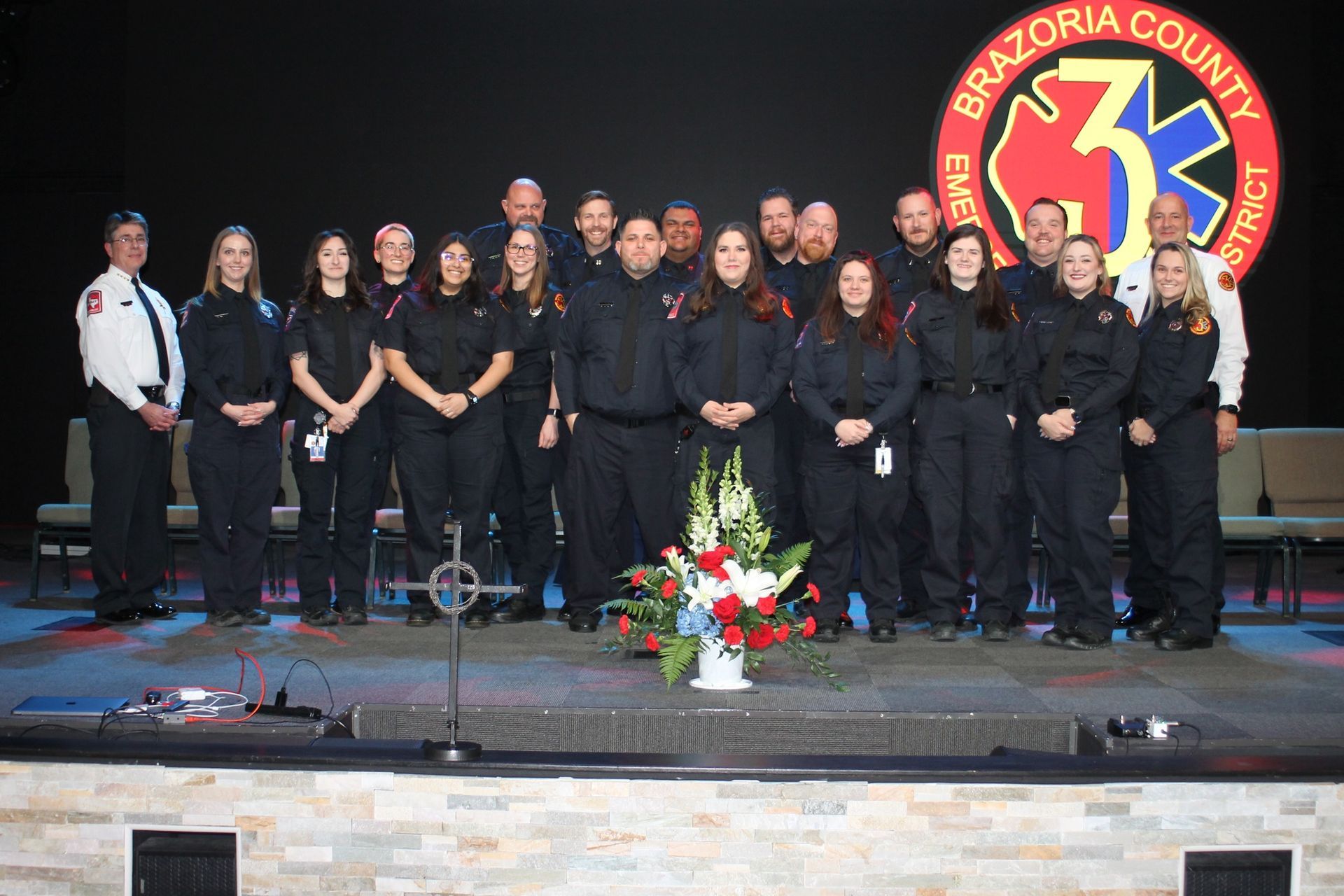 Group of emergency medical services personnel in dark uniforms, standing on a stage with Brazoria County logo