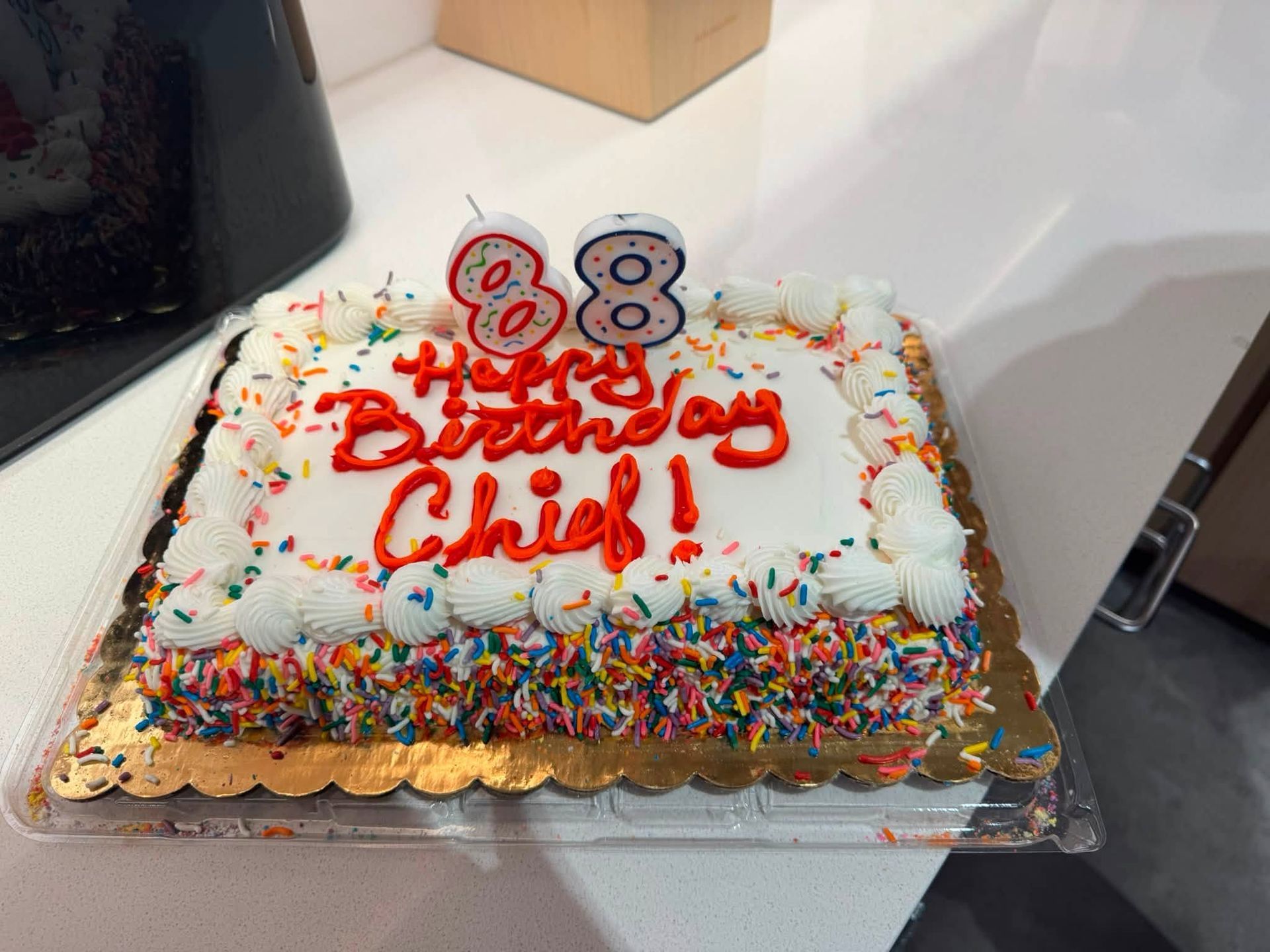 Birthday cake with colorful sprinkles and red frosting reading “Happy Birthday Chief!”