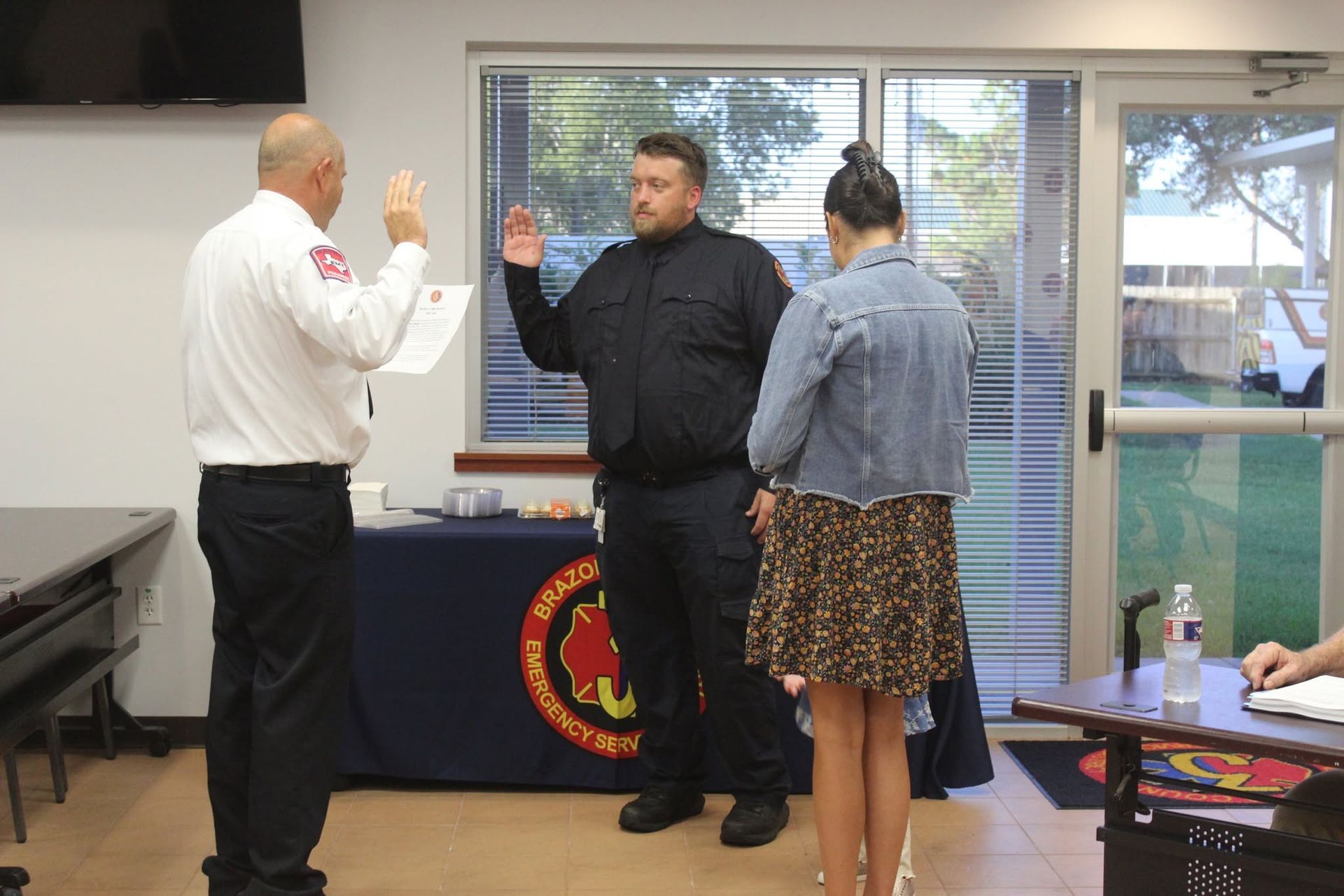 Three people stand at the front of a room with raised hands during a ceremony or pledge.