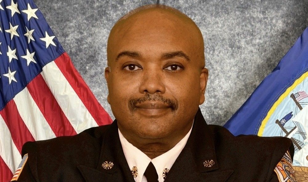 Fire chief in formal uniform seated at a desk, with U.S. and department flags behind him.