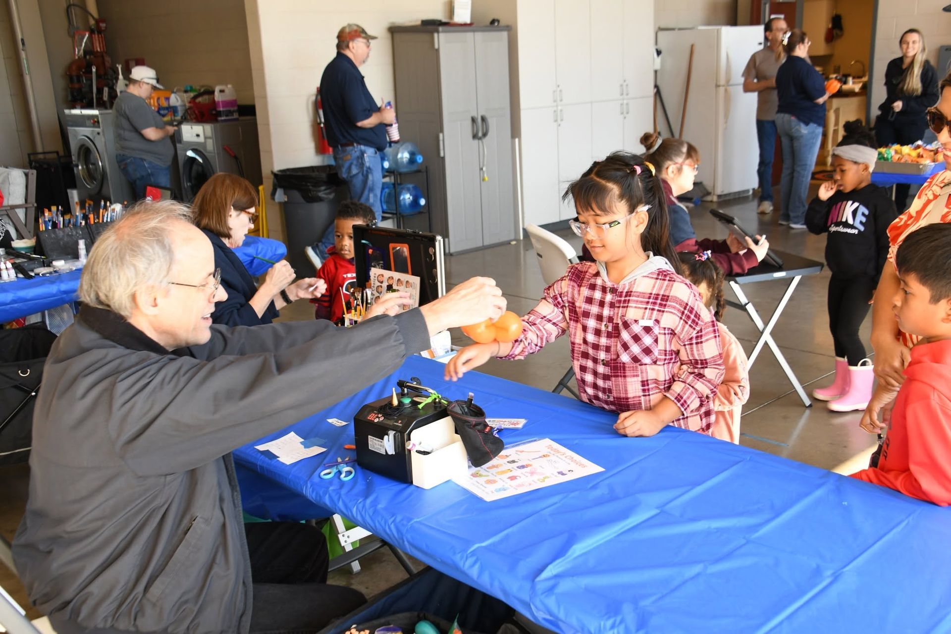 People sitting at a blue-tablecloth table making balloon art in a casual indoor gathering.