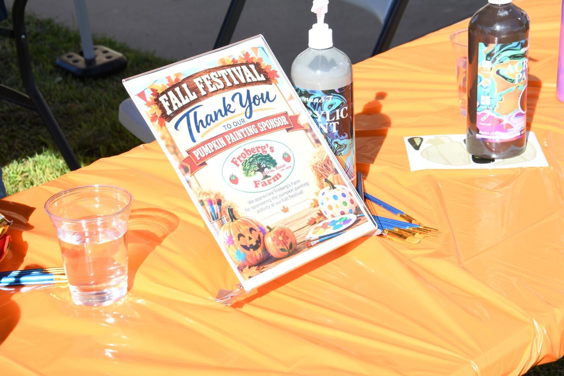 Orange tablecloth with flyers, a paint bottle for face painting at an outdoor fall festival booth.