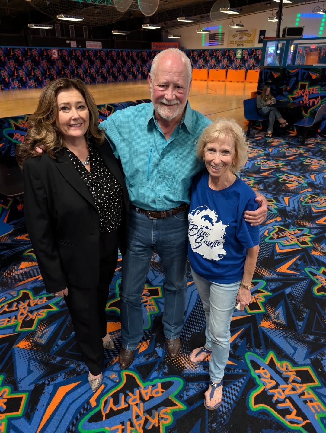 Three people posing together in a colorful bowling alley, smiling at the camera.