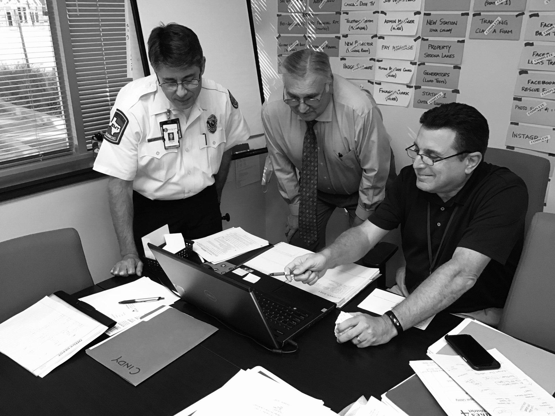 A black and white photo of three men looking at a laptop