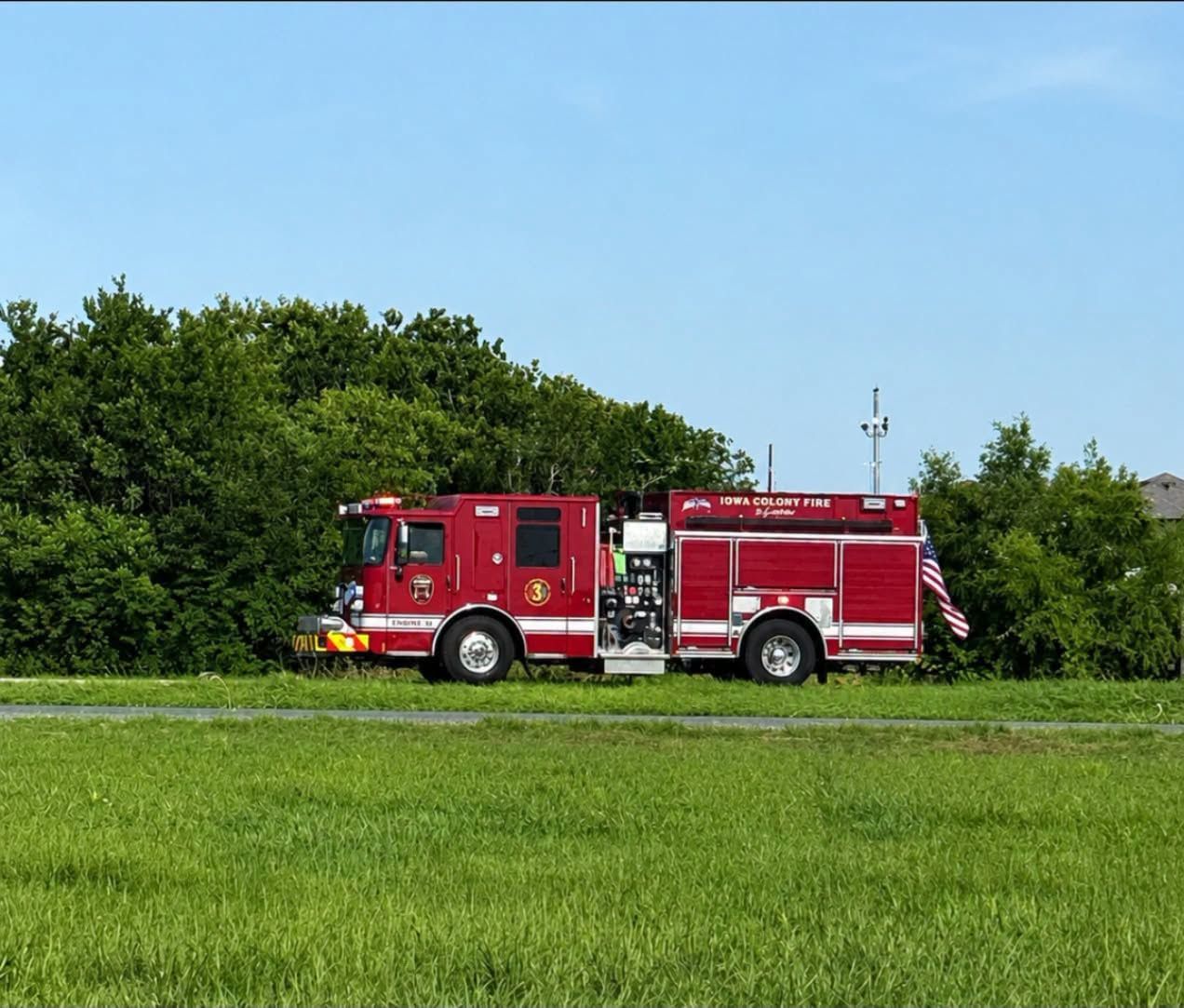 Red fire truck parked in a green field with trees under a blue sky