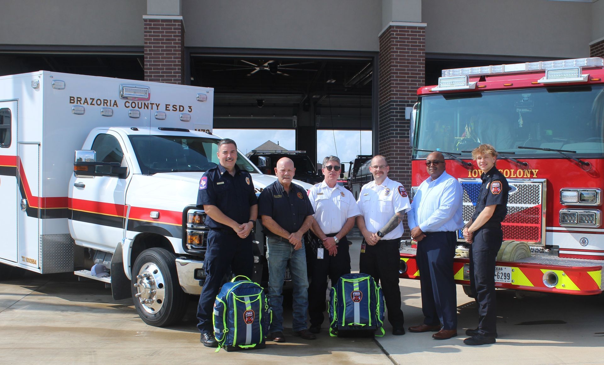 Firefighters and paramedics posing with rescue vehicles at a fire station entrance