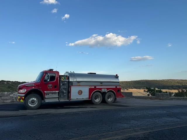 Red fire tanker truck parked on a roadside under a blue sky